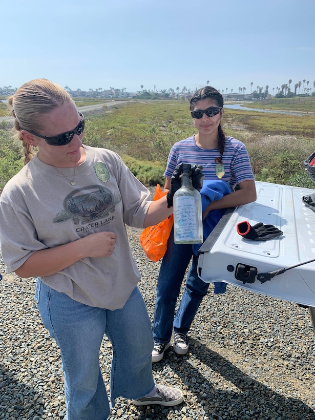 Cal State Fullerton roommates Elleanna Mauck, left, and Emily Moreno display a message in a bottle found during a volunteer cleanup of the Santa Ana River Marsh, Sept. 23, in Newport Beach, Calif.