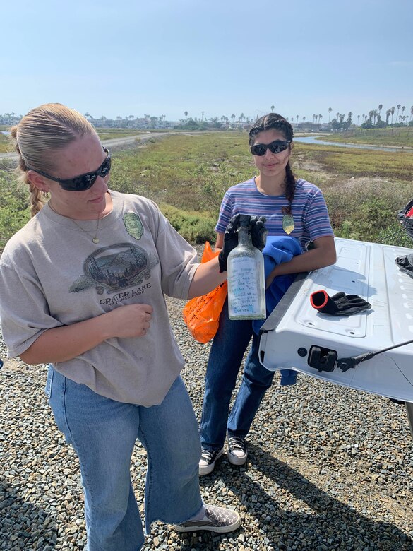 Cal State Fullerton roommates Elleanna Mauck, left, and Emily Moreno display a message in a bottle found during a volunteer cleanup of the Santa Ana River Marsh, Sept. 23, in Newport Beach, Calif.