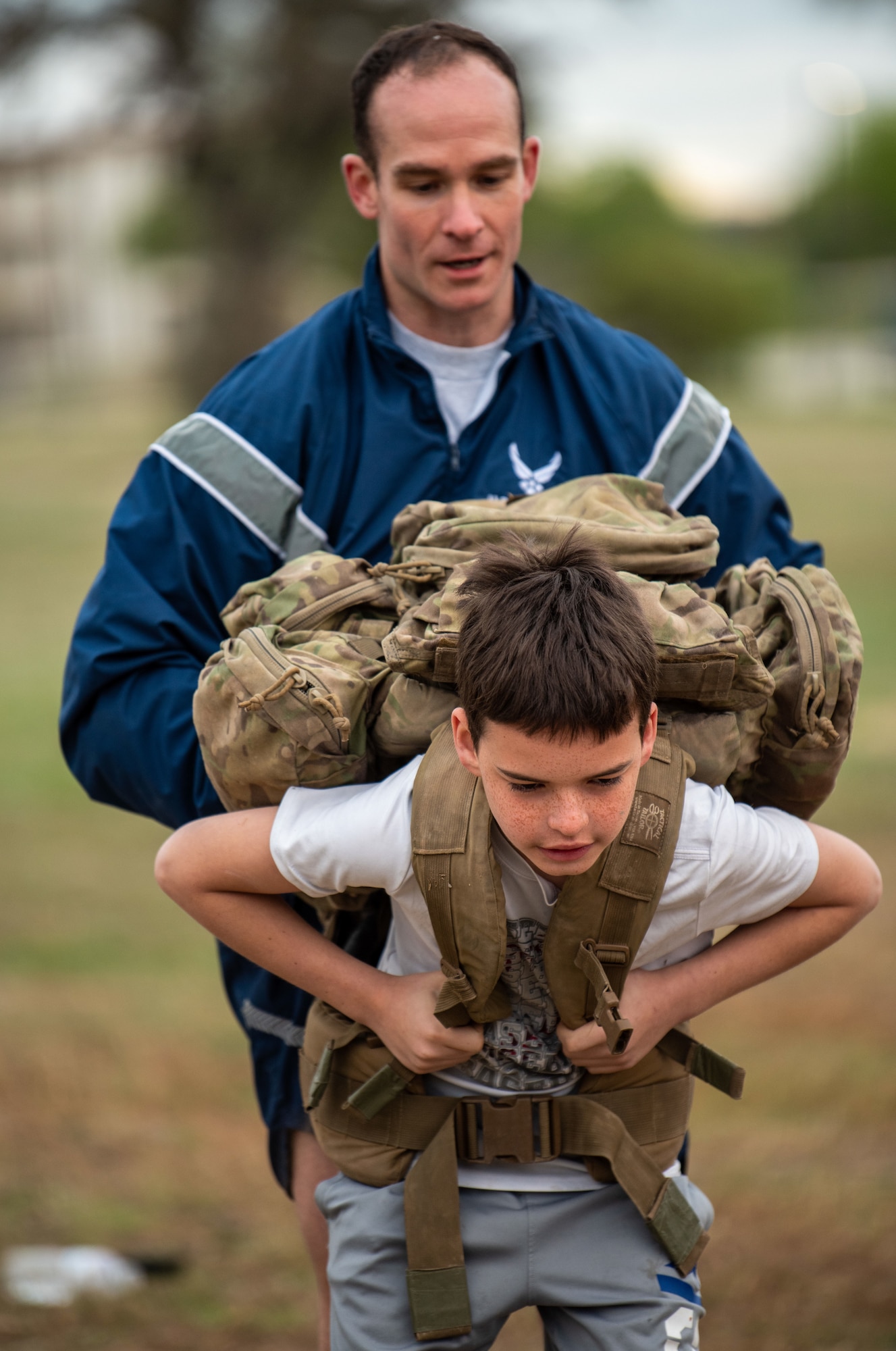 A TACP student helps a Boy Scout wiggle into a tactical backpack.