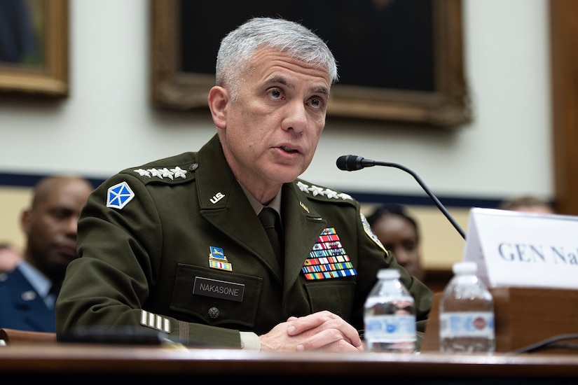 A service member in uniform sits at a table with a microphone.