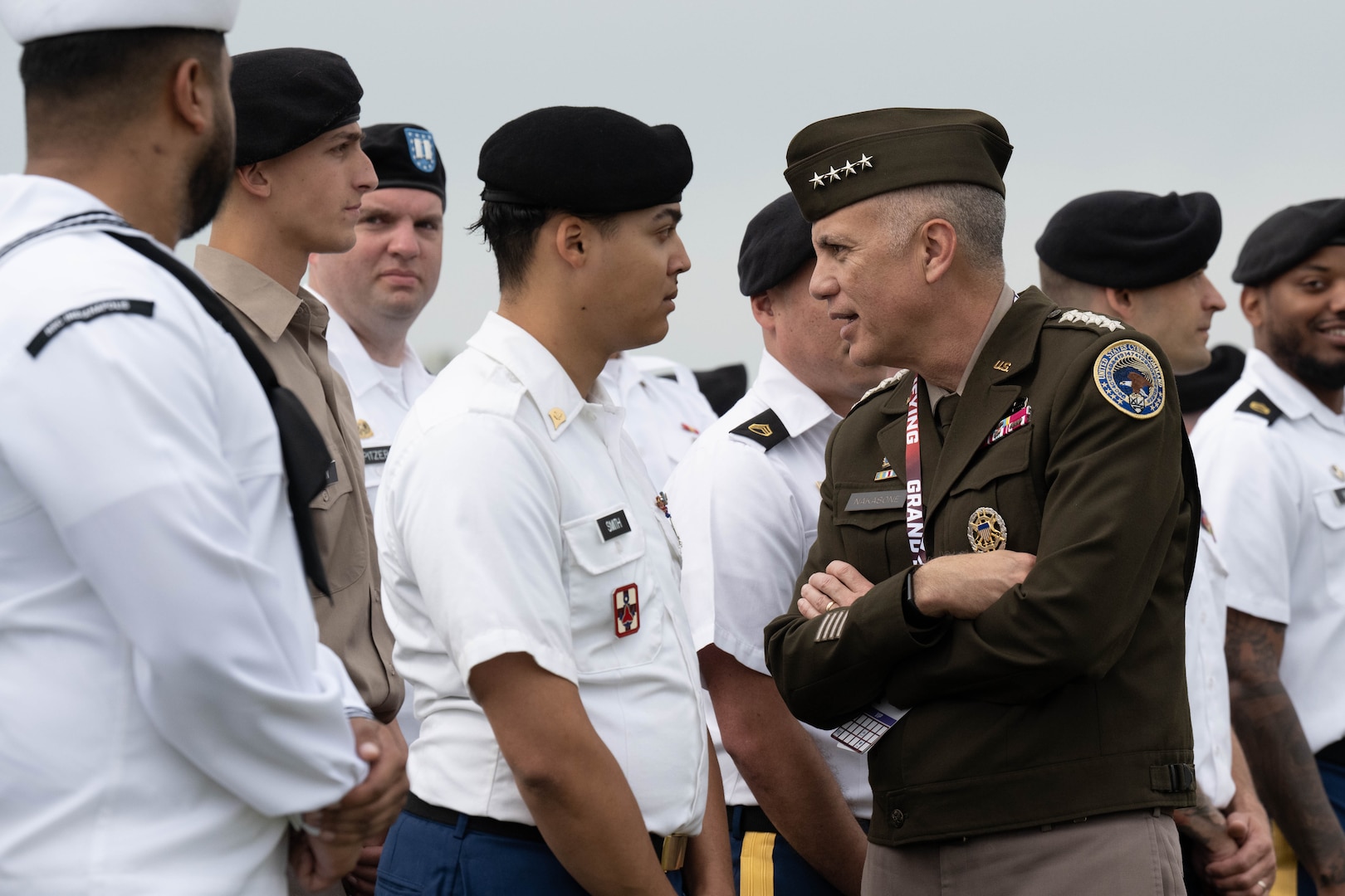 Two service members in uniform converse while standing near a group of men also in uniform.