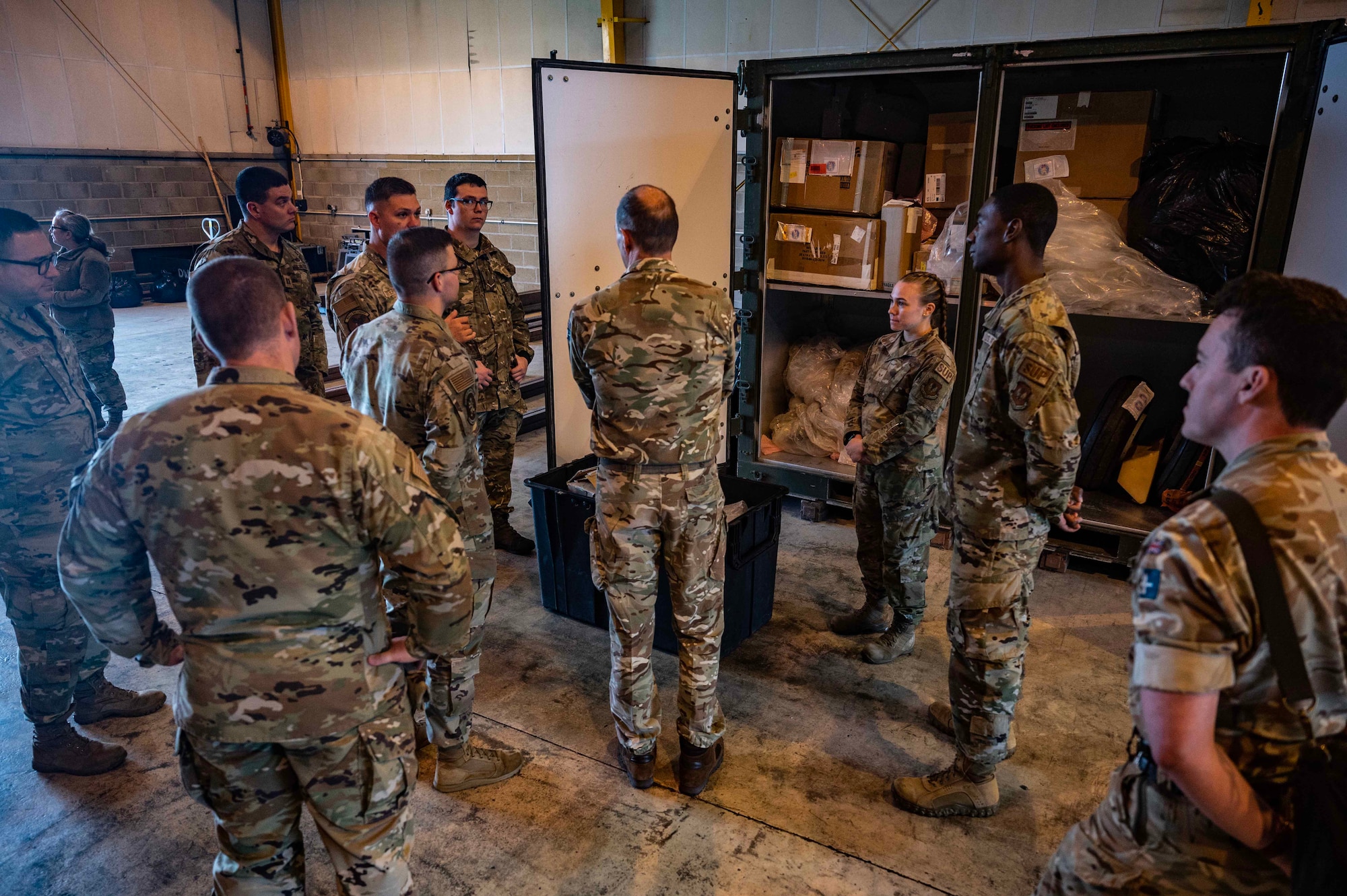 British Army Brigadier Timothy Crossland, 102nd Operational Sustainment Brigade commander, center, learns about the cargo deployment function during a base tour at Royal Air Force Mildenhall, England, Sept. 28, 2023. Crossland visited RAF Mildenhall to educate Airmen about the 102nd OSB, learn more about the base’s cargo deployment function, and highlight Airmen from the CDF. (U.S. Air Force photo by Senior Airman Viviam Chiu)