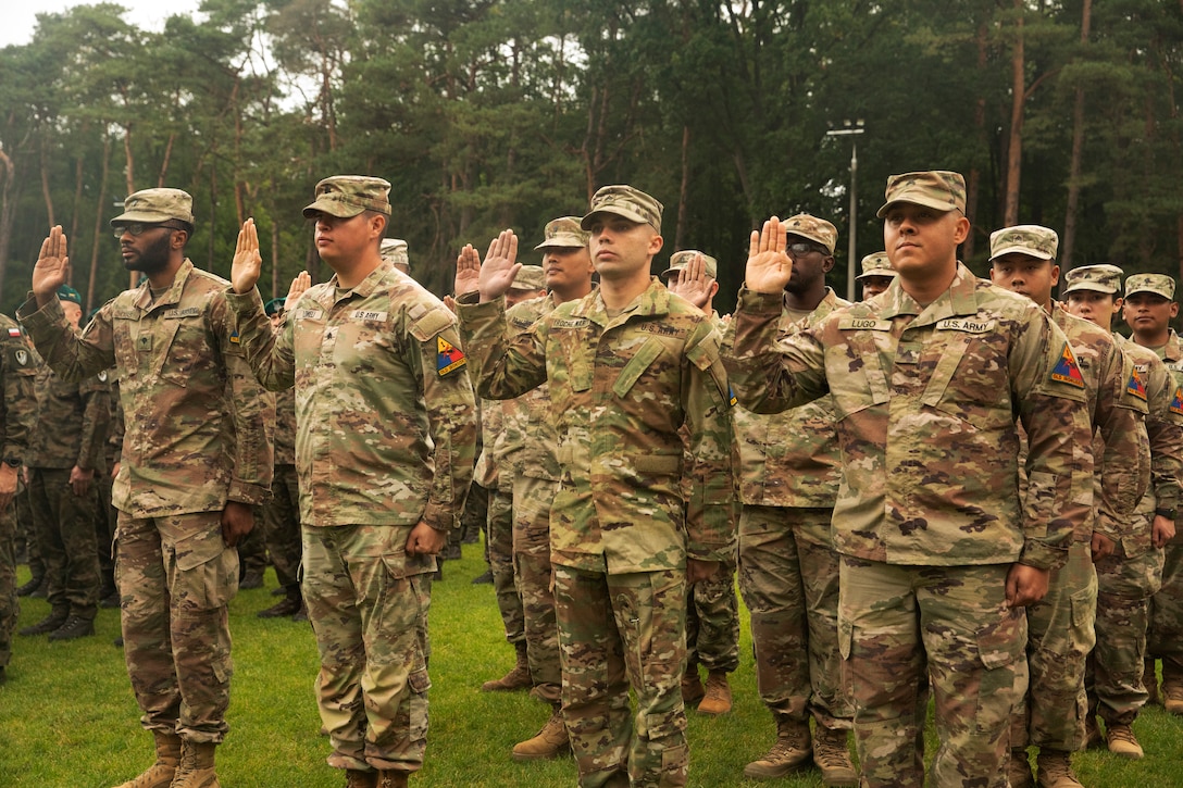 Soldiers stand in formation with their right hands raised and recite the oath of enlistment during a joint formation with Polish soldiers.