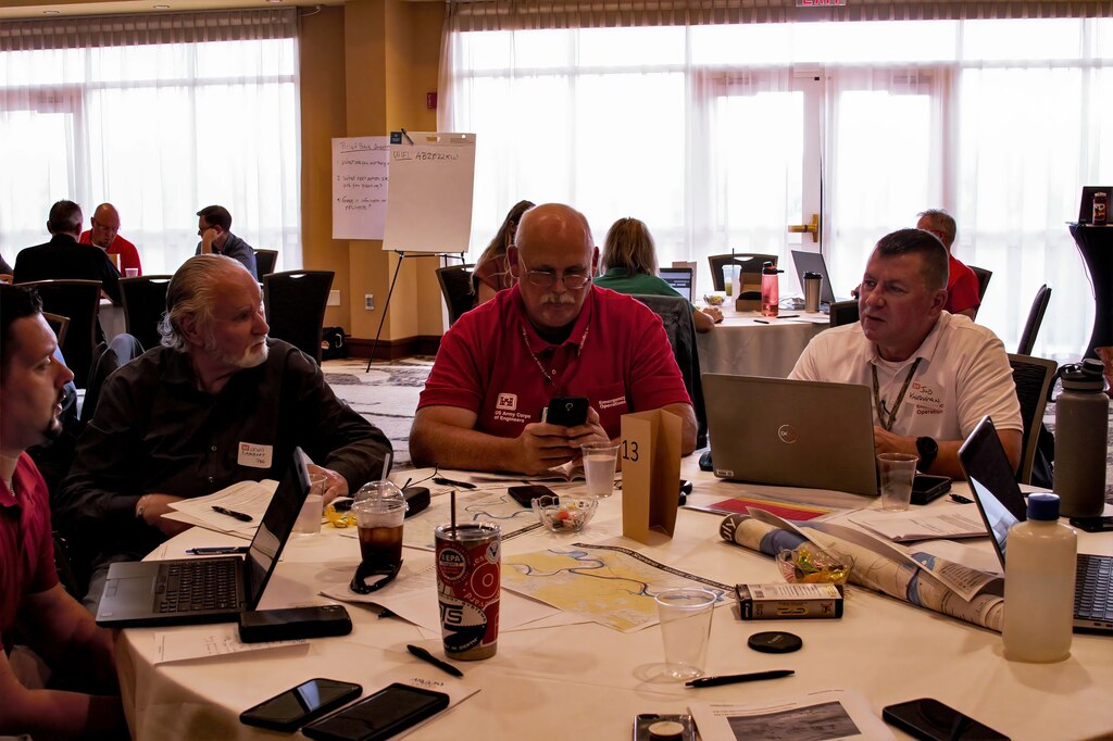 Four men sit at a round table with computers and notepads.