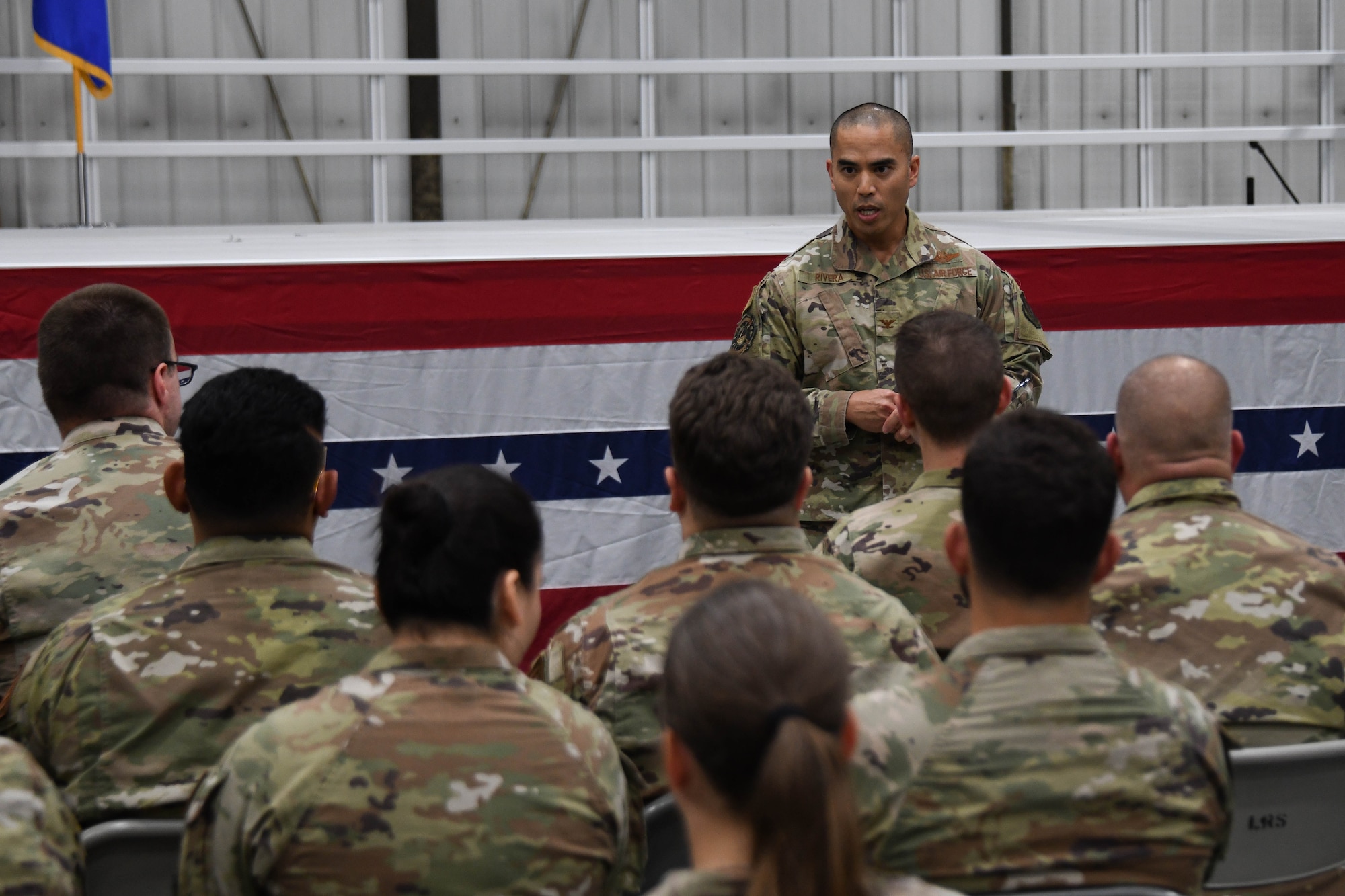 A man in a military uniform talks to a group of military members.