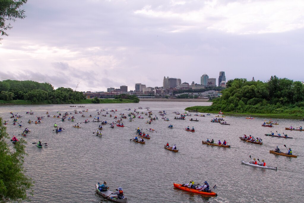 Many kayaks can be seen on the river with the Kansas City skyline in the background.