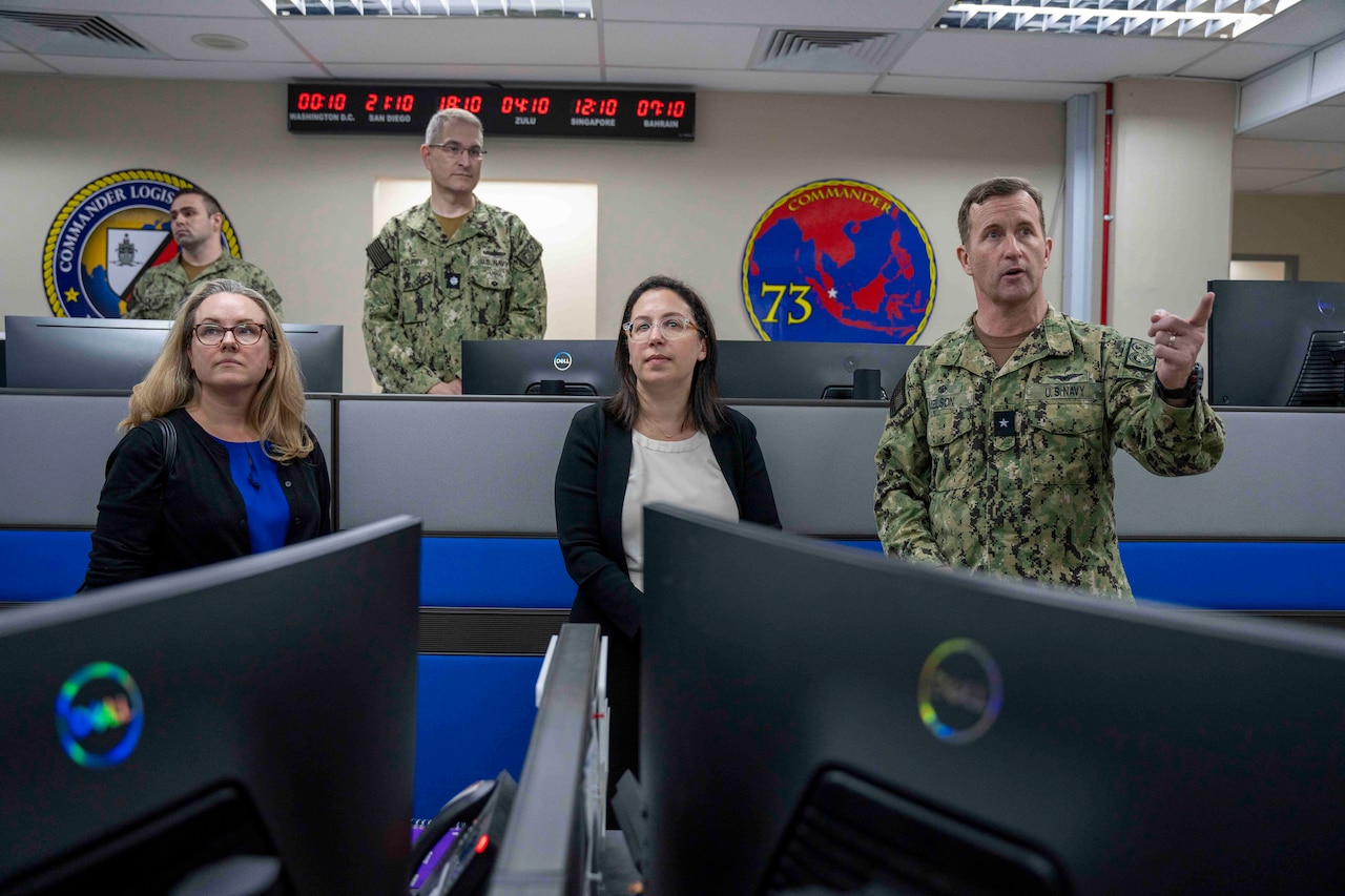 Five people stand while looking on in a government operations center.
