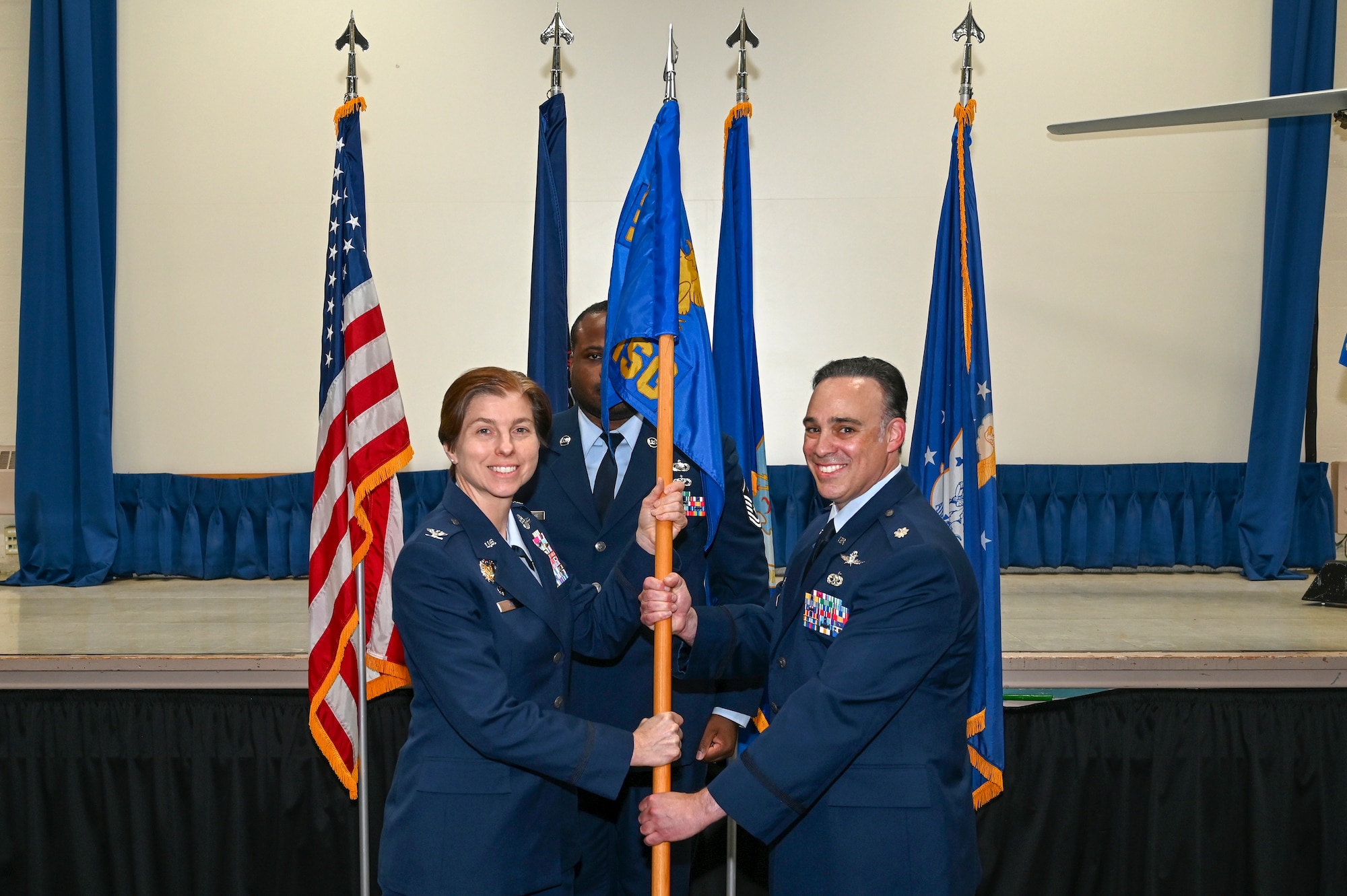 A woman in U.S. Air Force dress blues poses for a photo with a man in USAF Dress Blues holding a guidon.