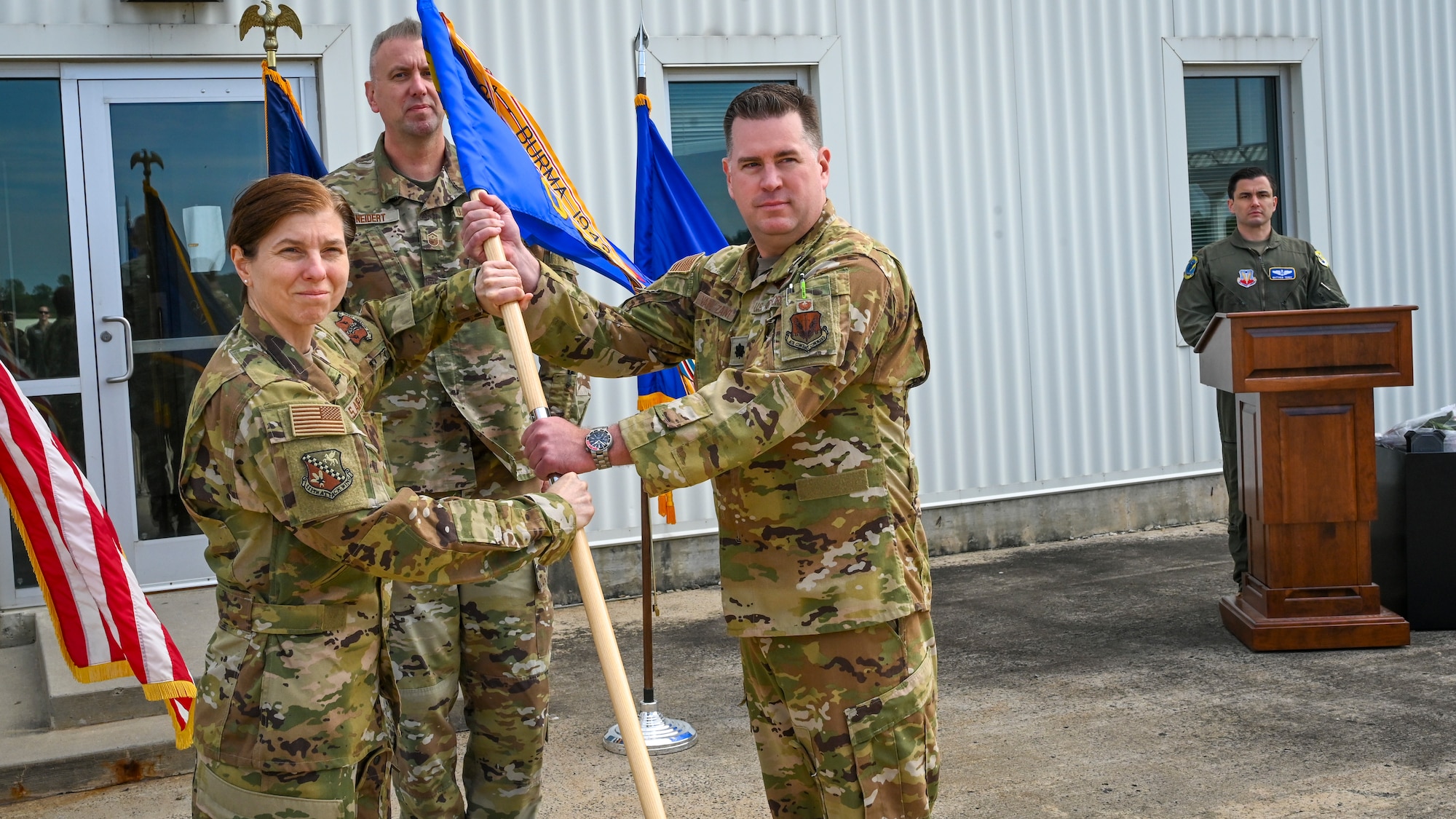 A man and woman in USAF uniforms pose for a photo holding a guidon during a change of command ceremony.