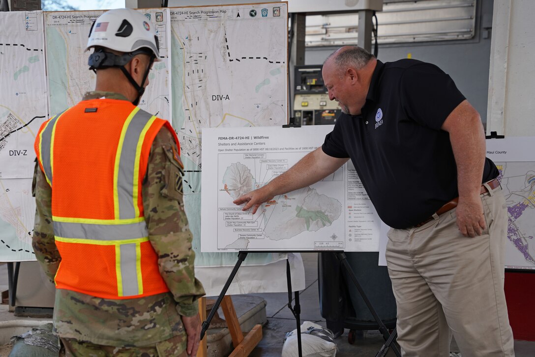 A man shows information on a chart to another man wearing a hard hat and safety gear.