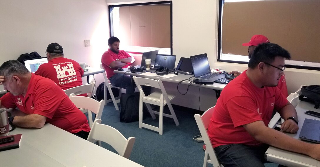 Five men wearing U.S. Army Corps of Engineers Emergency Operations shirts work in an office setting.