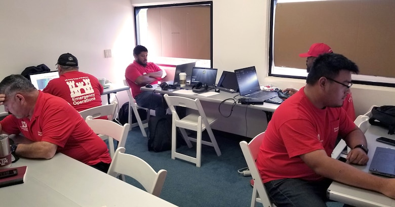 Five men wearing U.S. Army Corps of Engineers Emergency Operations shirts work in an office setting.