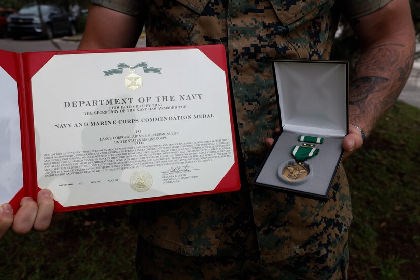 A Marine holds onto an award and a metal.