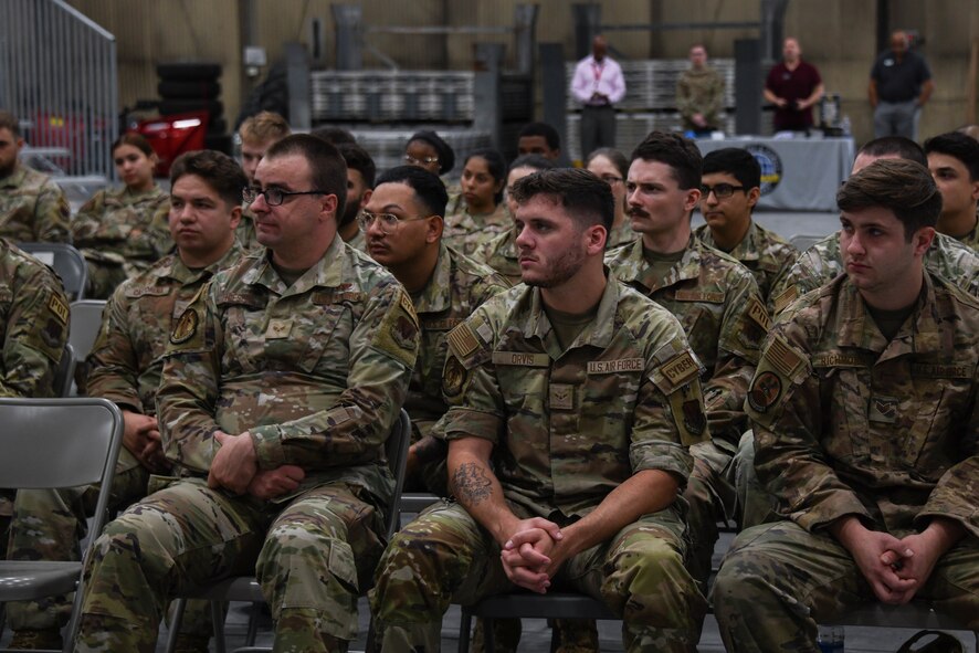 A group of military members sit in rows of chairs.
