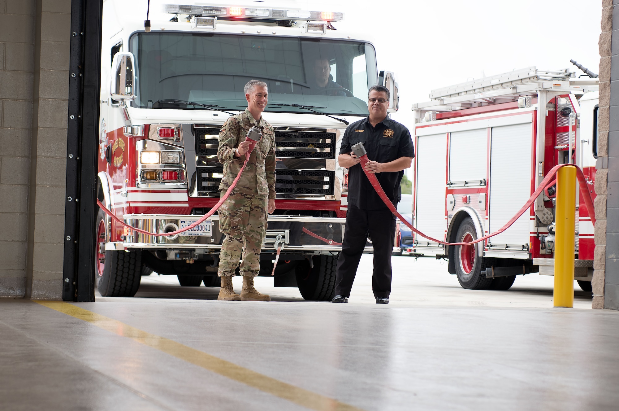 Two men holding a fire hose in front of a rescue truck.