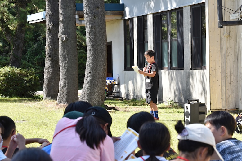 A child stands with a microphone in his hand to recount his English Camp memories to a listening audience.