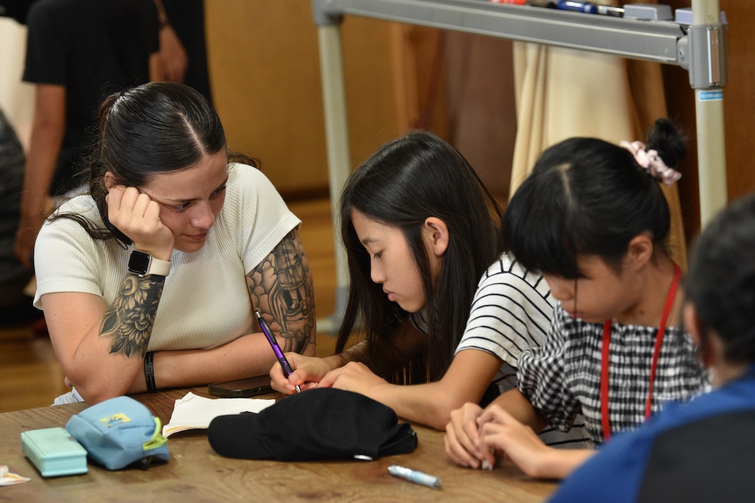 Corporal Sarah Malka, a company guide assigned to CATC Camp Fuji, watches over a child as she writes a short speech about her experiences during English Camp, September 18, 2023. CATC Camp Fuji Marines mentored Japanese children through English Camp emersion course hosted by the National Chuo Youth Friendship Center in Gotemba, Japan.  (U.S. Marine Corps photo by Song Jordan)