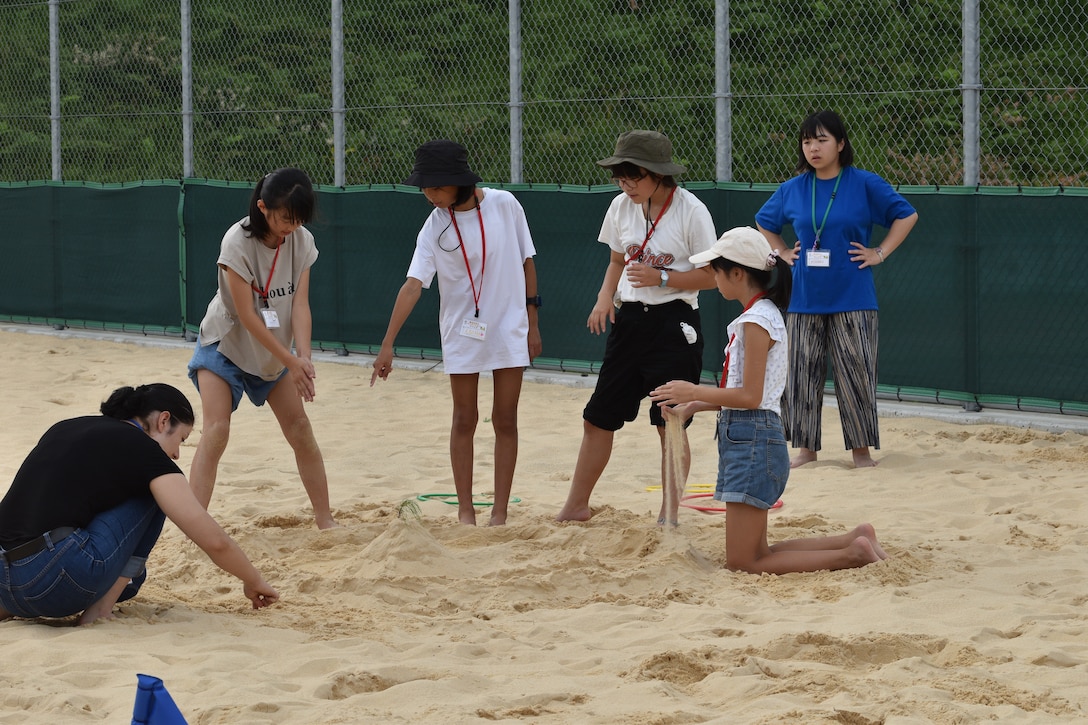 Corporal Brissenia Rojo, from the CATC Camp Fuji range control office, plays in the sand with girls, September 16, 2023. CATC Camp Fuji Marines mentored Japanese children through English Camp emersion course hosted by the National Chuo Youth Friendship Center in Gotemba, Japan. (U.S. Marine Corps photo by Song Jordan)