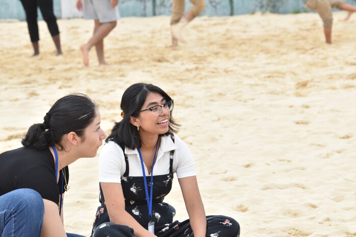 Sergeant Selene Cruz Alavez and Cpl. Brissenia Rojo sit in the sand as they interact with youth.