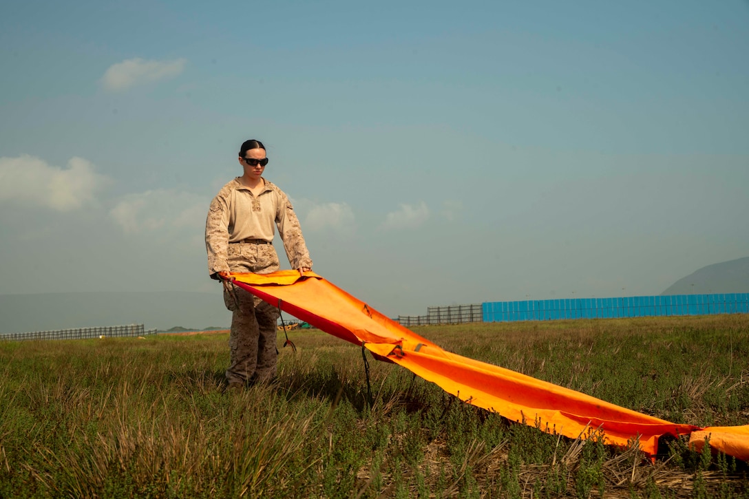 A Marine places a large  orange marker in the middle of a large field.