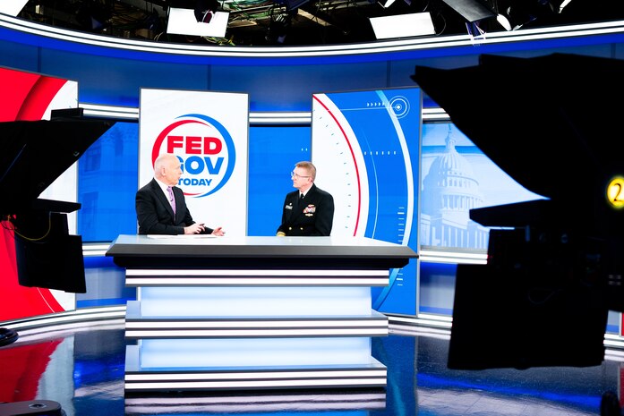 The Director fo U.S. Navy Strategic Systems Programs (SSP) Vice Adm. Johnny R. Wolfe, Jr (right) sits on the news set for Fed Gov Today and talks with host Francis Rose (left), Sunday. You can see the TV cameras in the photo. Rose and Vice Adm. Wolfe are sitting side-by-side at a news desk. In the background is the red, white, and blue show set that has the show's logo on it. The logo reads "Fed Gov Today" and is contained within a half-blue-half-red circle. Vice Adm. Wolfe highlighted SSP's focus on the workforce with new employee onboarding programs like 'SSP Now' and how the initiatives equip the workforce to support SSP's nuclear deterrence mission and support America's Warfighting Navy. SSP is the command that provides cradle-to-grave lifecycle support for the sea-based leg of the nation's nuclear triad.