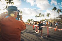 A race spectator photographs runners during the Marine Corps Base Hawaii Na Ali’i 5K/10K held on MCBH, March 16, 2024. Headquarters Battalion, MCBH, co-hosted the annual race and is one of 12 races part of the MCBH Commanding Officer’s Semper Fit Race Series. (U.S. Marine Corps photo by Lance Cpl. Dezmond Browning)