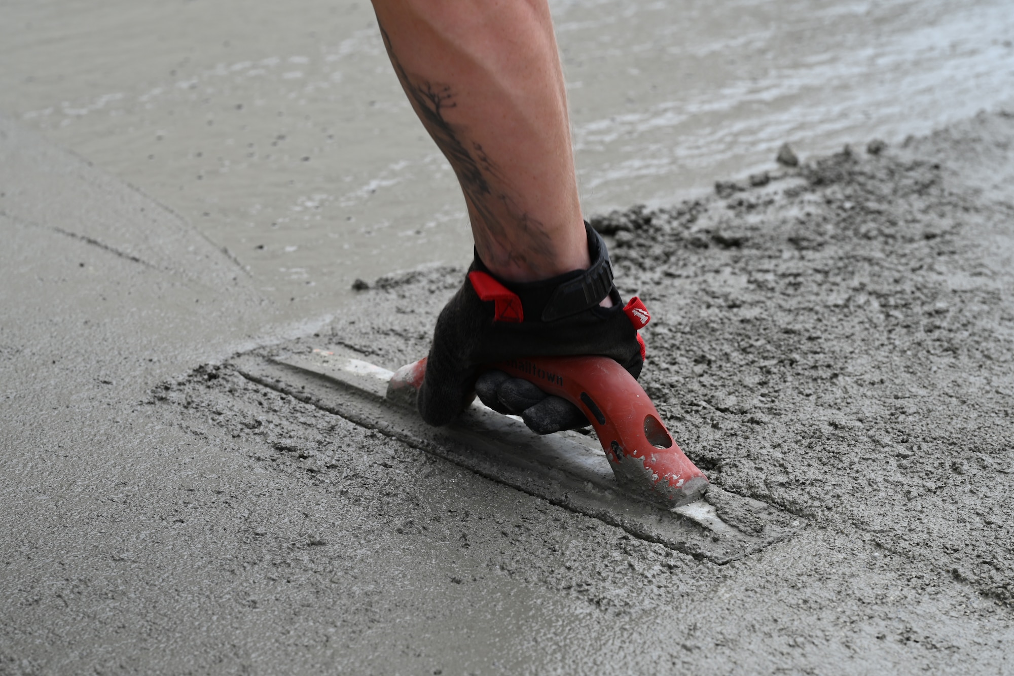 An Airman is using a magnesium float to push the coarse aggregate down and smooth out the concrete mixture.