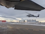 Framed by the tail of a 211th Rescue Squadron HC-130J Combat King II, a 210th Rescue Squadron HH-60G Pave Hawk, carrying 212th Rescue Squadron Guardian Angel personnel recovery Airmen, sorties from Unalakleet, Alaska, March 21, 2024. The HH-60 transloaded Guardian Angels to the HC-130 before continuing to Kotlik for a medical evacuation mission.