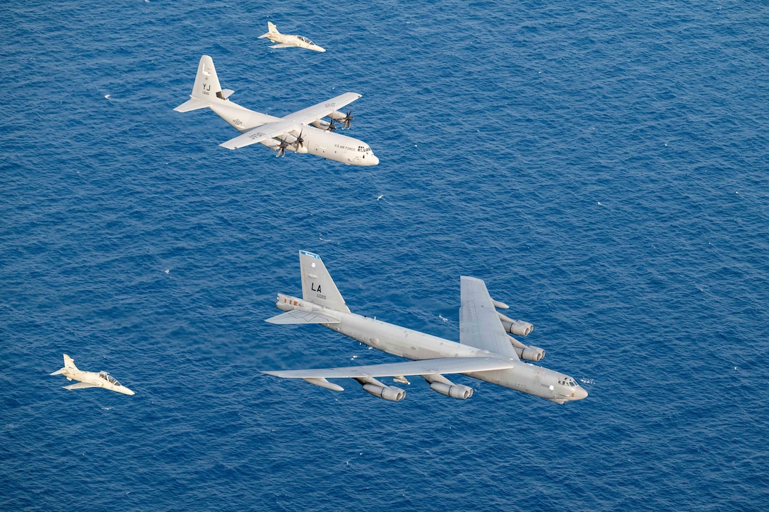 Four military aircraft fly in formation above blue water.