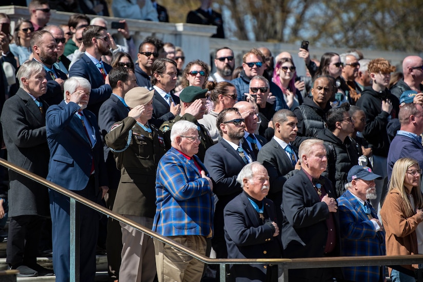 A group of people salute and place their hands over their hearts.