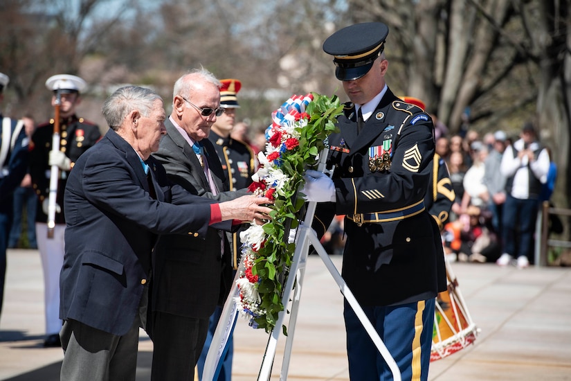 Two civilians and a military officer hold a wreath.