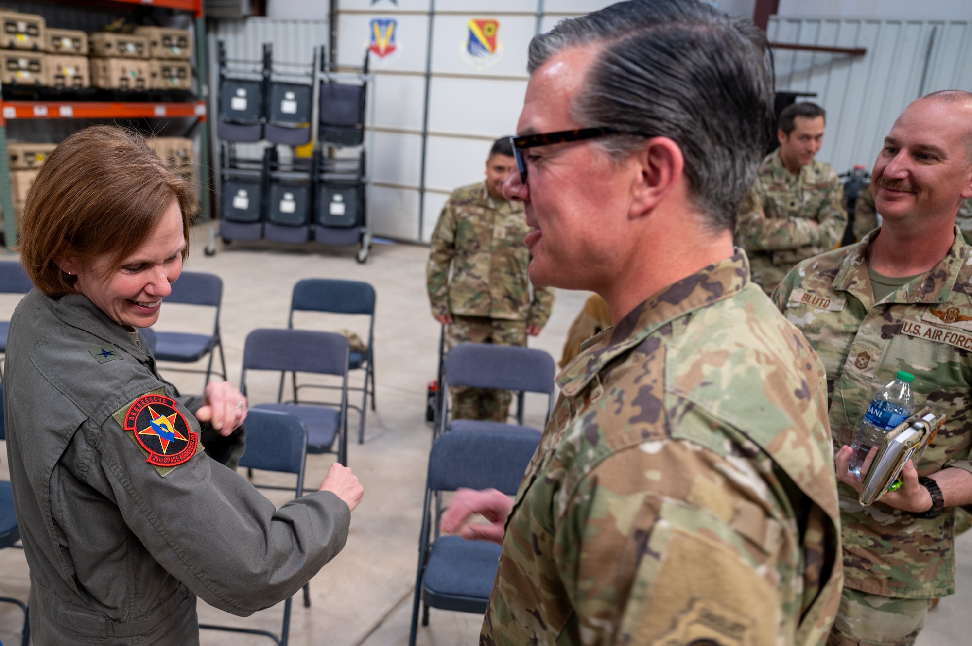 A woman wearing a U.S. Air Force military uniform looks at a military patch on her arm while others look on.