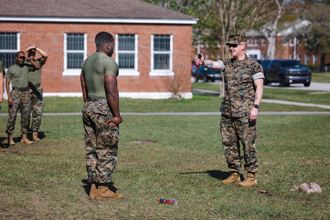 U.S. Marine Corps Pfc. Jeremiah Hall, left, an administrative specialist, gets sprayed with oleoresin capsicum (O.C.) spray by Gunnery Sgt. Jeremie Burd, a substance abuse control officer, both with Headquarters and Support Battalion, Marine Corps Installations East-Marine Corps Base (MCB) Camp Lejeune, during a React Force Training course on MCB Camp Lejeune, North Carolina, March 29, 2024. The O.C. spray training strengthened the Marines’ ability to suppress a threat in the event of being exposed to the substance. (U.S. Marine Corps photo by Lance Cpl. Loriann Dauscher)