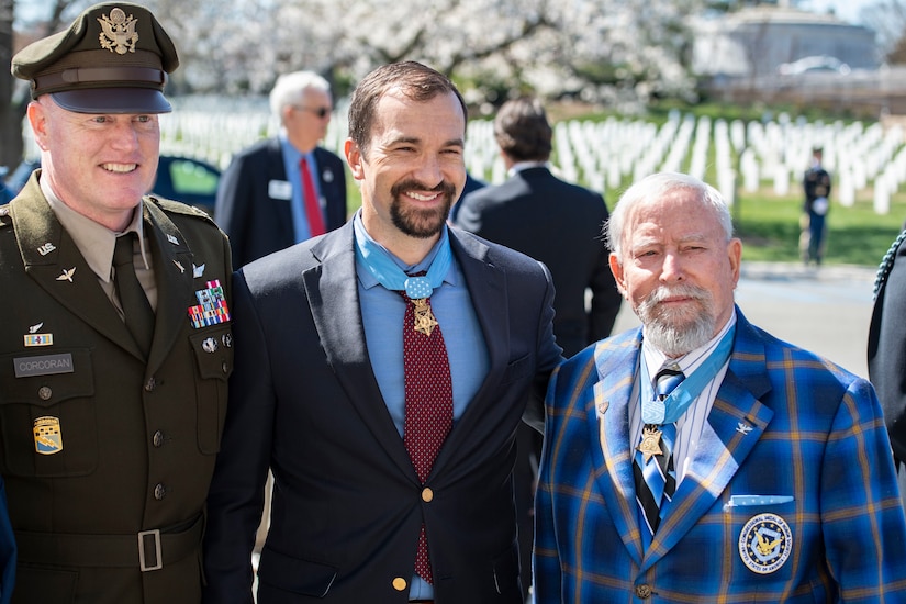 A military officer and two civilians wearing medals pose for a picture.