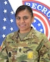 Female Soldier in Army uniform poses in front of United States and Army Recruiting Command flags.