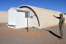 A Soldier pointing at a Quonset hut.