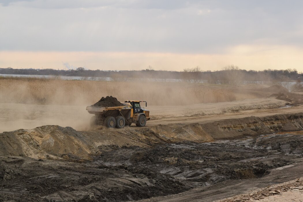 Photo shows a dump truck hauling sediment along a dike/dirt road. 