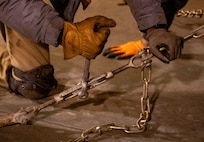 A photo of a man securing a vehicle with chains.
