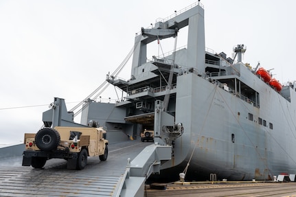A photo of two Humvees driving up the ramp of a ship.