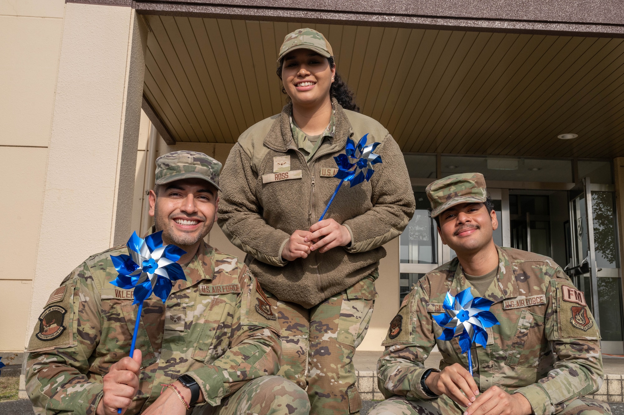Three Airmen pose for a phot and hold pinwheels.