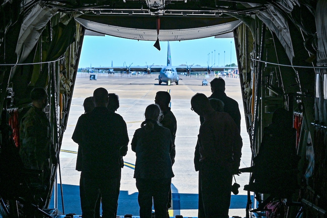 Nine people stand inside of a C-130J Super Hercules with a C-130J Super Hercules in the background