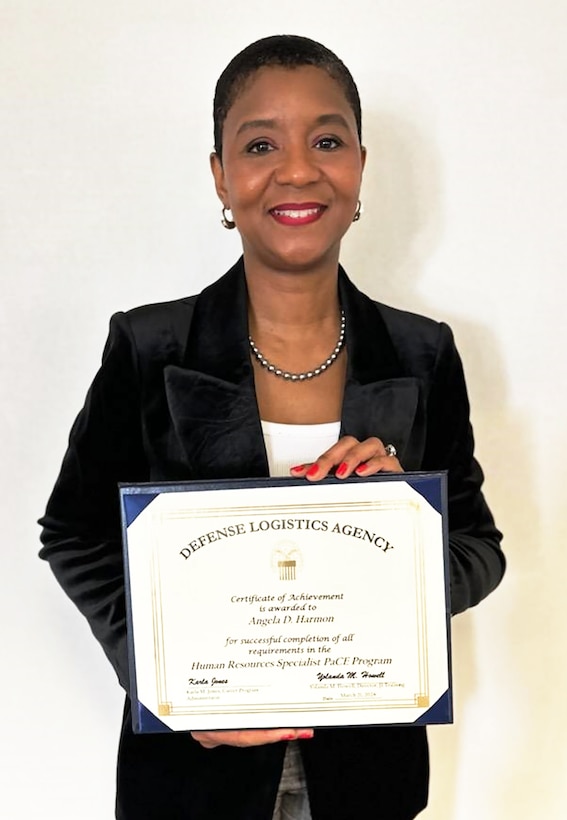 Black woman stands against a wall holding a certificate
