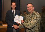 Jason Payne, Office of Naval Research Director of Global Tech Solutions, present the Navy and Marine Corps Achievement Medal to Lt. Cmdr. Samuel Hughes, NAS Patuxent River Air Traffic Control Facility Officer, for superior performance of his duties in supporting the Air Traffic Control training simulation technology development with the Office of Naval Research Global Tech Solutions from 2021 to 2022.
Hughes was commended for taking initiative to improve trainee achievement of NATOPS standards and objectives by motivating the science and technology community to develop a dedicated training system to allow air traffic control radar operators to conduct uninterrupted training sessions. The solution reduced the training timeline and increased the quality of instruction to significantly increase mission readiness.