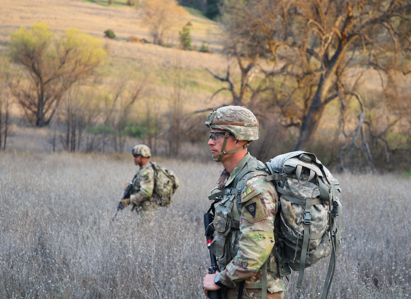 Staff Sgt. Roger Dyer watches hand and arm signals, as the squad’s march through the brush to simulate evacuating a casualty as part of the Best Squad Competition. Five members of the 80th Training and its three divisions joined together to compete in the 2024 Best Squad competition hosted by the 63rd Readiness Division in Camp Parks and Fort Hunter Liggett, Ca.