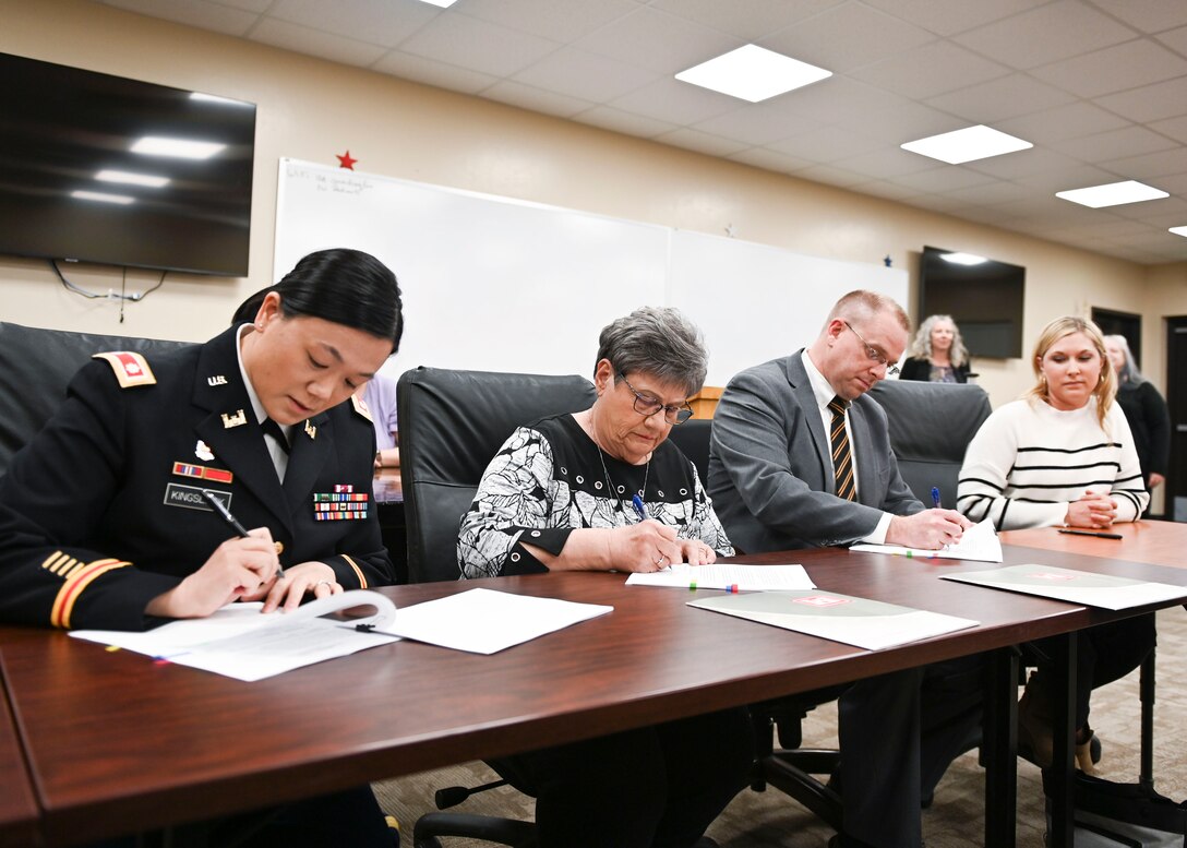 four people sitting at a table, signing documents