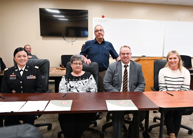 four people sitting at a table. One person standing behind.