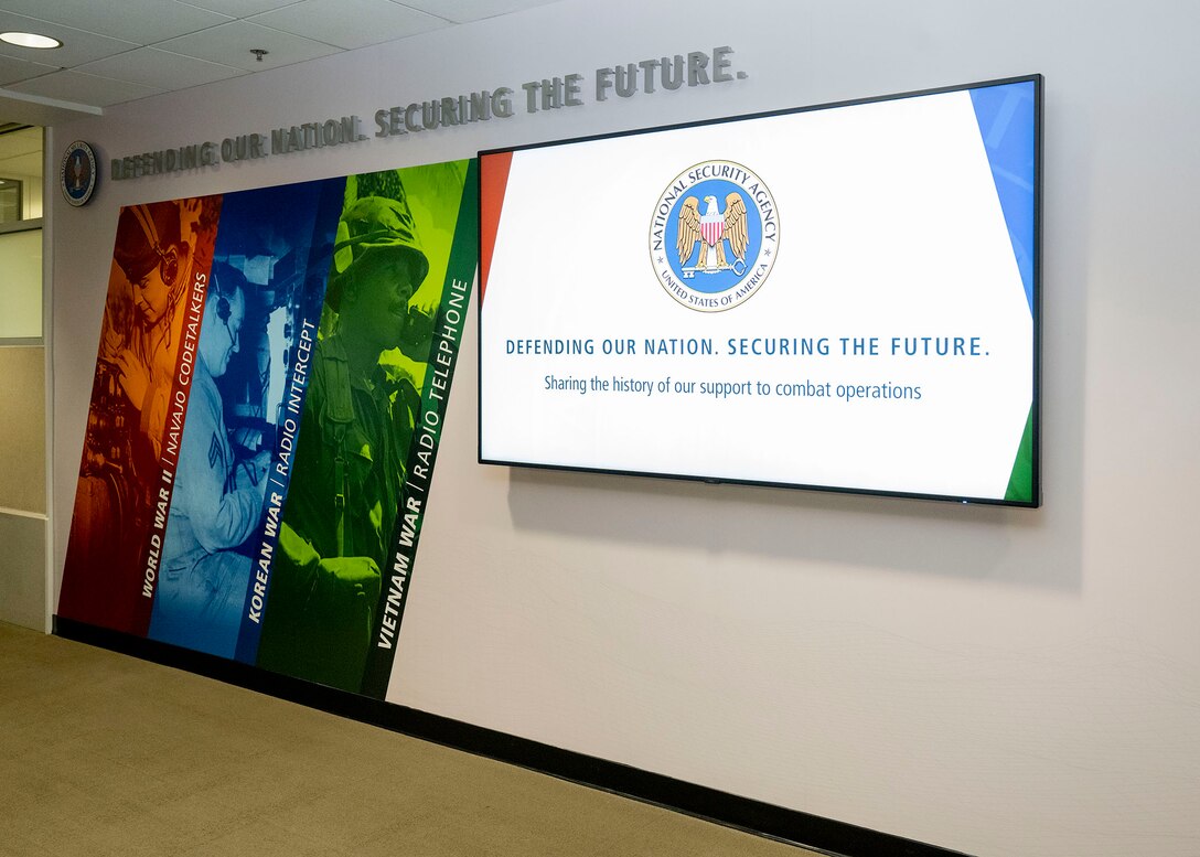 The display at BWI. Three panels (orange, blue, and green) include images of cryptologists during WWII, the Korean War, and the Vietnam War. A screen features a slideshow of images from SIGINT operations during these times.