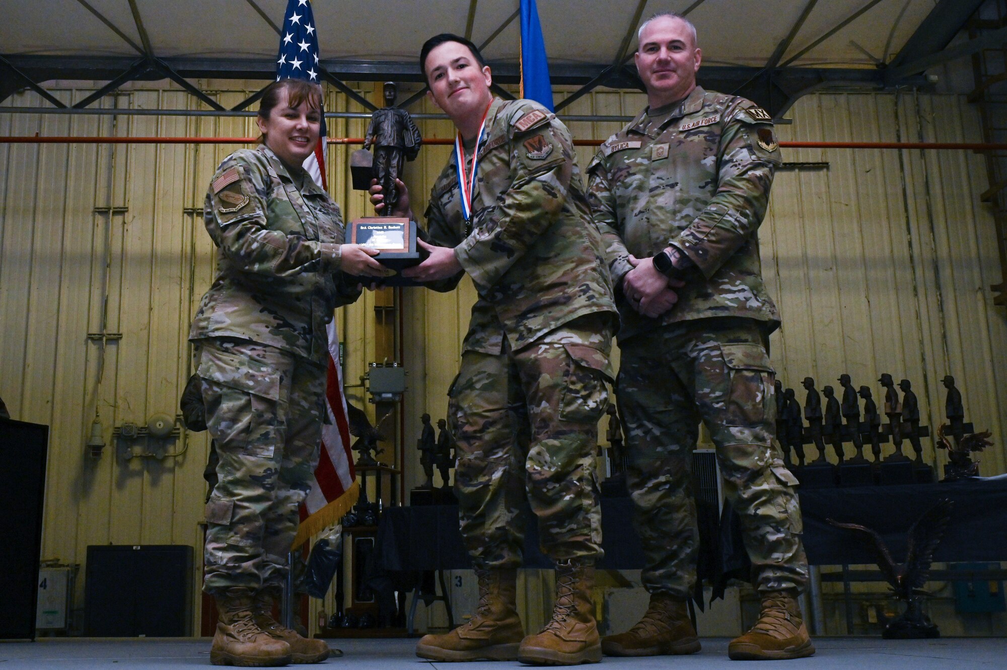 Senior Airman Christian Sackett, center, assigned to the 335th Fighter Generation Squadron, receives the Specialist of the Year award from Col. Kathryn Roman, 4th Maintenance Group commander and Chief Master Sgt. Michael Bylica, 4 MXG senior enlisted leader, during the 4 MXG Maintenance Person of the Year ceremony at Seymour Johnson Air Force Base, North Carolina, Mar. 08, 2024. The MPOY ceremony recognized 37 Airmen from multiple maintenance career fields and highlighted their accomplishments. (U.S. Air Force photo by Airman Rebecca Tierney)