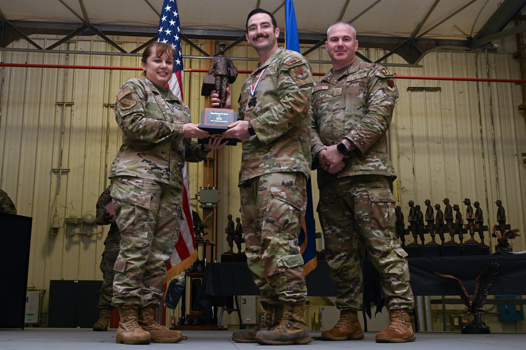 Tech. Sgt. Cameron Green, center, assigned to the 335th Fighter Generation Squadron, receives the Specialist of the Year award from Col. Kathryn Roman, 4th Maintenance Group commander and Chief Master Sgt. Michael Bylica, 4 MXG senior enlisted leader, during the 4 MXG Maintenance Person of the Year ceremony at Seymour Johnson Air Force Base, North Carolina, Mar. 08, 2024. The MPOY ceremony recognized 37 Airmen from multiple maintenance career fields and highlighted their accomplishments. (U.S. Air Force photo by Airman Rebecca Tierney)