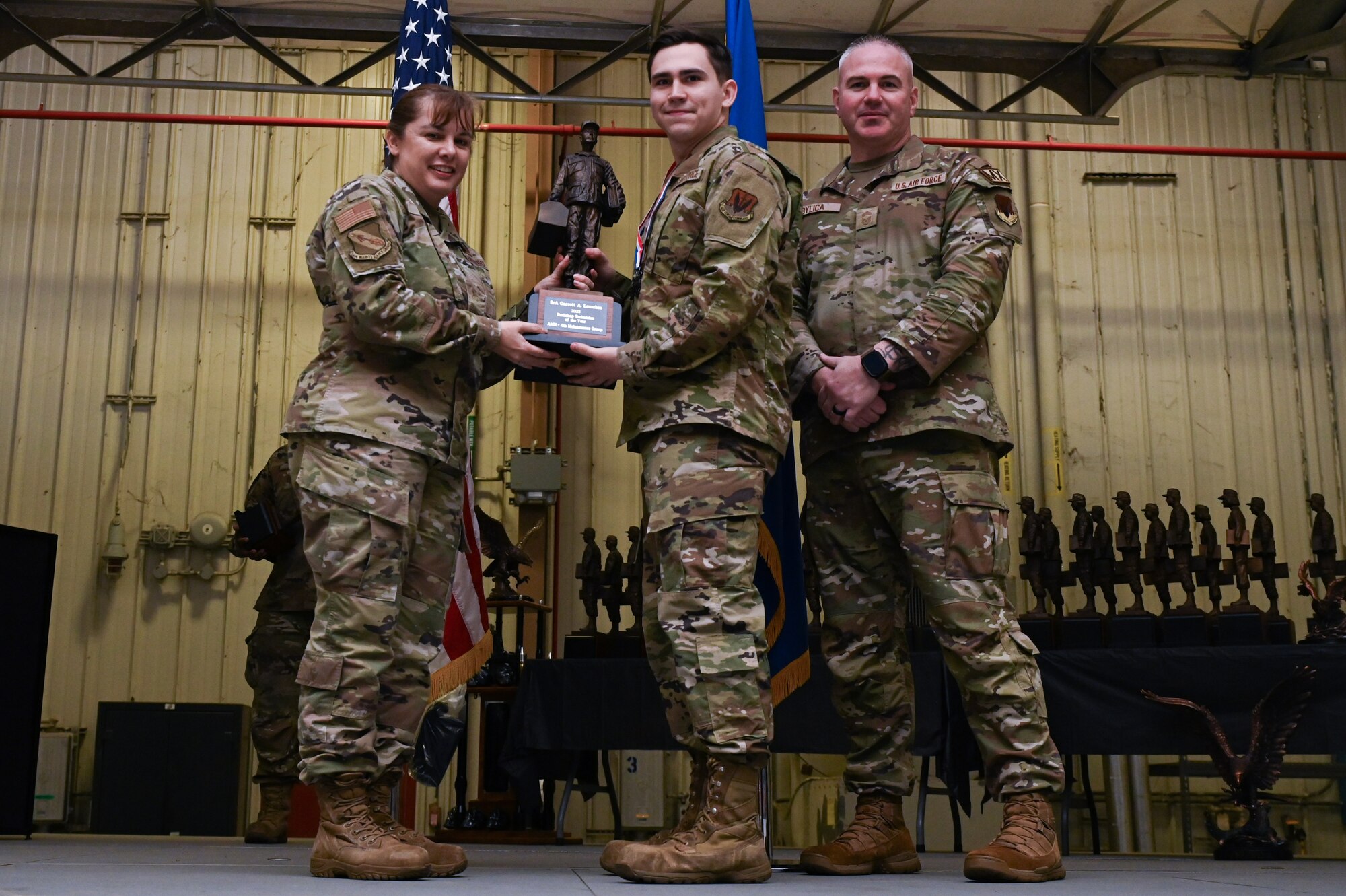Senior Airman Garrett Loeschen, center, assigned to the 4th Component Maintenance Squadron, receives the Back-shop Technician of the Year award from Col. Kathryn Roman, 4th Maintenance Group commander and Chief Master Sgt. Michael Bylica, 4 MXG senior enlisted leader, during the 4 MXG Maintenance Person of the Year ceremony at Seymour Johnson Air Force Base, North Carolina, Mar. 08, 2024. The MPOY ceremony recognized 37 Airmen from multiple maintenance career fields and highlighted their accomplishments. (U.S. Air Force photo by Airman Rebecca Tierney)